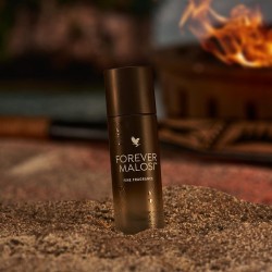 Flacon de Forever Malosi Fine Fragrance posé sur le sable avec un feu en arrière-plan - Parfum boisée épicée pour hommes